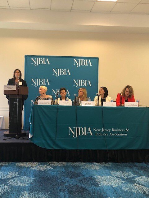 Filomena along with other women at a panel listening to a woman on a mic.